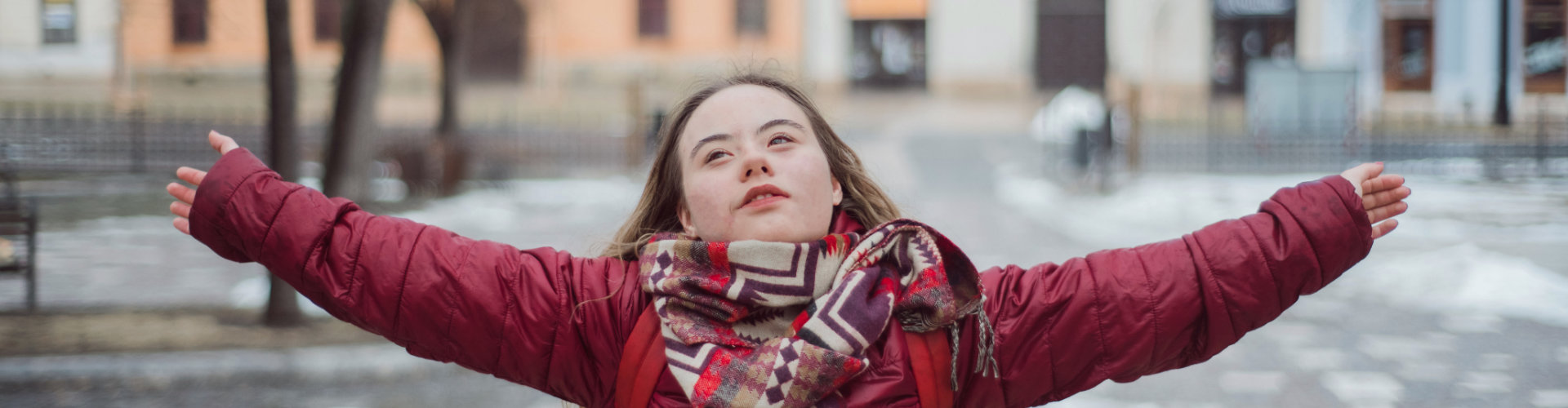 Junge Frau mit Down-Syndrom breitet fröhlich die Arme aus