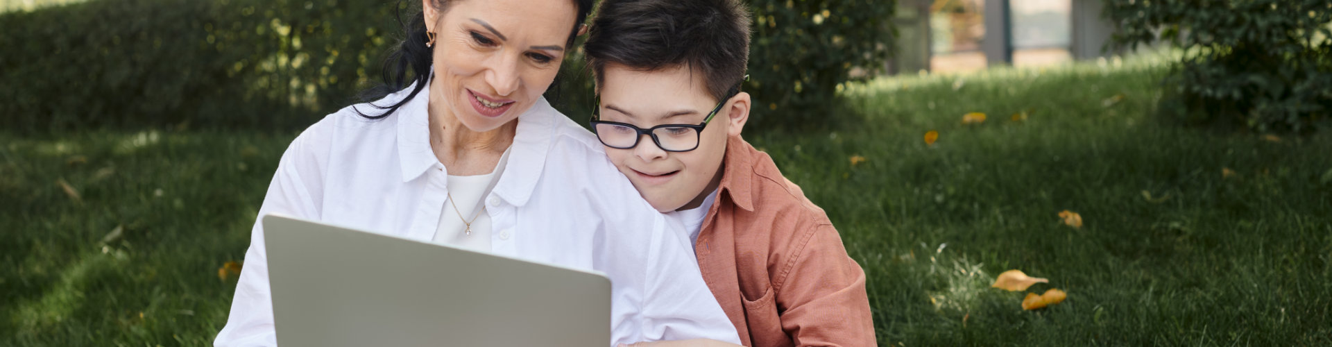 Junge mit Down-Symdrom schaut mit seiner Mutter auf einen Computer